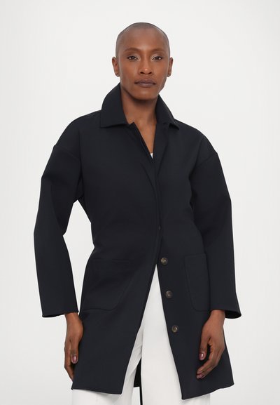 Ναυτικό μπλε παλτό μέχρι το γόνατο φτιαγμένο από χοντρό ύφασμα. Διαθέτει ζωντανό γιακά, μπροστινό κλείσιμο με κουμπιά και δύο μπροστινές τσέπες. Φαρδιές μανσέτες με άνετη εφαρμογή.