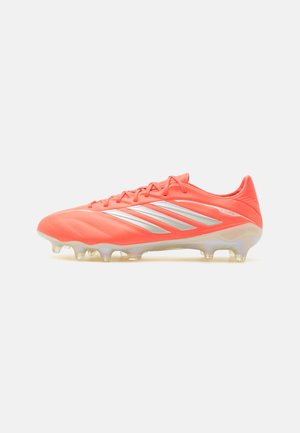 Fel koraalkleurige Adidas voetbalschoen met zilveren strepen, gevormde noppen en veterluiting, zijaanzicht op witte achtergrond.