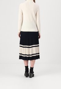 Pletený krémový svetr s vysokým límcem, kombinovaný s námořnickou plisovanou sukní s krémovými a námořnickými pruhy. Viditelné masivní černé boty na blokovém podpatku.