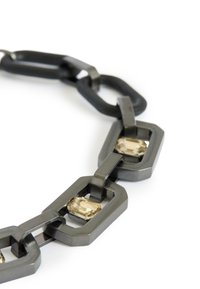 Metal chain necklace features elongated, interlocking geometric links in dark gray with two faceted light amber stones embedded.