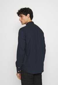 Marineblaues Langarmhemd mit Kragen, geknöpften Manschetten und glatter Textur. Es zeichnet sich durch ein minimalistisches Design, eine maßgeschneiderte Passform und dezente Steppnähte aus.