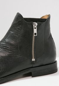 Mustat nahka nilkkasaappaat, joissa on sivuvetoketju, sileä pinta, pyöreä kärki ja pinottu korko vakauden takaamiseksi.