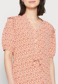 Abito floreale con scollatura a V, maniche a palloncino corte e vita legata. Presenta un motivo floreale nei colori rosa, arancione e giallo su un tessuto leggero.