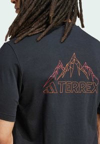 Čierne bavlnené tričko s geometrickou grafikou hory v oranžovej a červenej farbe na chrbte s textom "TERREX" pod ňou. Krátke rukávy, okrúhly výstrih.