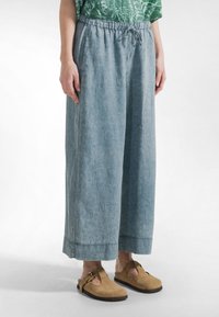 Lichtblauwe wijde broek van zachte stof met een elastische tailleband en koordsluiting. Heeft een relaxte pasvorm en omgeslagen zoom.