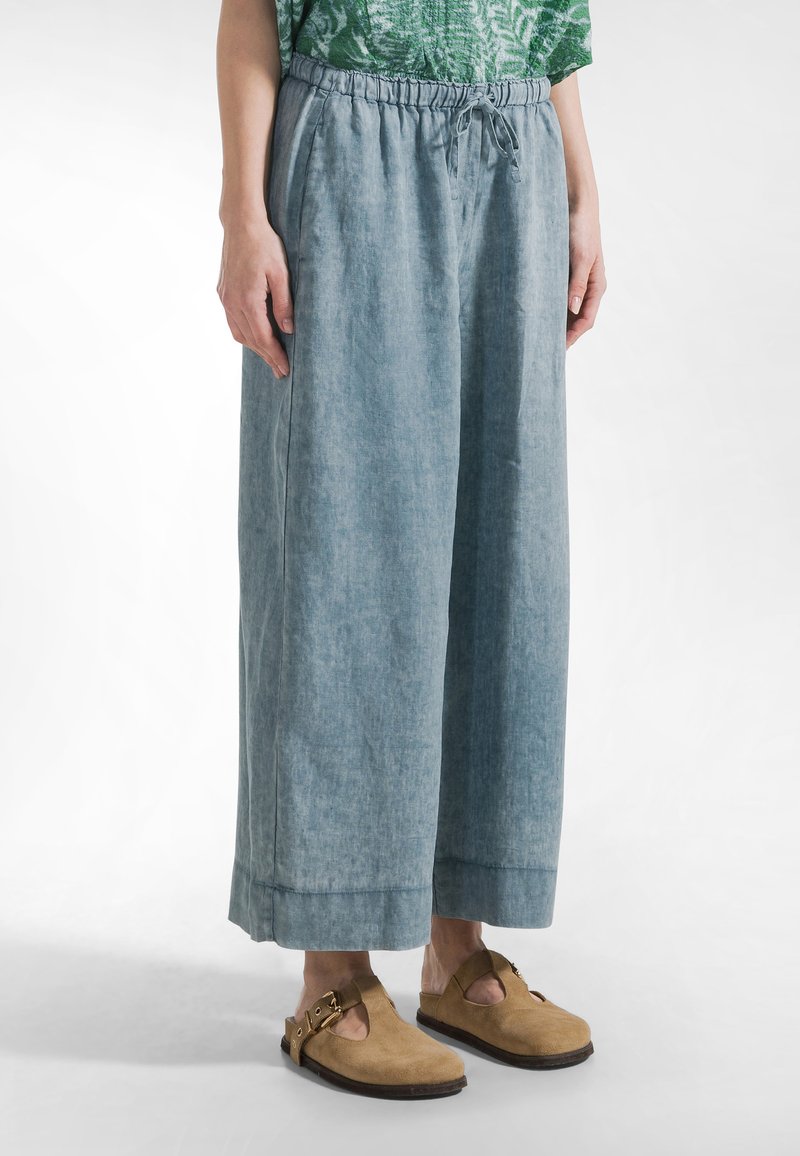 Lichtblauwe wijde broek van zachte stof met een elastische tailleband en koordsluiting. Heeft een relaxte pasvorm en omgeslagen zoom.