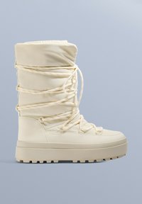 Buty wodoodporne w kolorze kremowym z pikowaną cholewką, krzyżowym sznurowaniem i grubą teksturowaną podeszwą. Wyposażone w okrągły nos i wyściełany kołnierz.