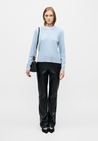 Light blue sweater with a ribbed neckline, paired with black faux leather trousers. Notable details include a fitted design and pointed-toe black shoes.