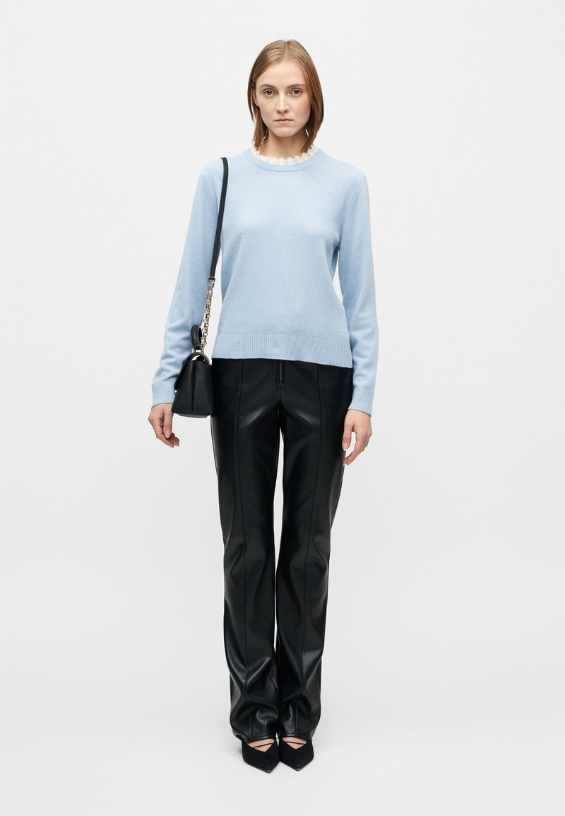 Light blue sweater with a ribbed neckline, paired with black faux leather trousers. Notable details include a fitted design and pointed-toe black shoes.