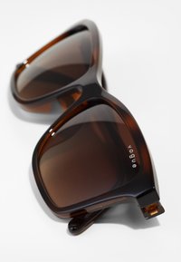 Ochelari de soare din material tortoise cu lentile pătrate supradimensionate, cu nuanță de maro în gradient și un logo subtil "vogue" pe ramă. Material plastic durabil.