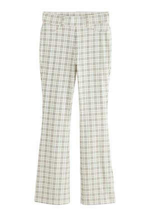 Frau trägt übergroßes Jeanshemd, weiße karierte Hose, braune Sandalen und hält eine braune Fransen-Clutch vor hellem Hintergrund.