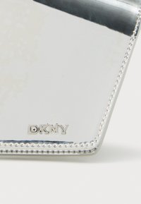 Ασημένιο πορτοφόλι από δερμάτινο υλικό με λογότυπο DKNY. Διαθέτει κομψό σχεδιασμό και εμφανείς ραφές κατά μήκος των άκρων, που αντανακλούν το φως.