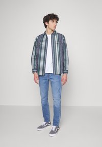 Striped button-up shirt with green and blue hues, white crew neck t-shirt, light blue jeans, and gray sneakers. Simple hardware details.