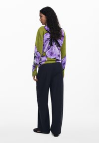 Green sweater with large purple floral pattern, long sleeves, paired with black wide-leg pants. Smooth texture, relaxed fit.