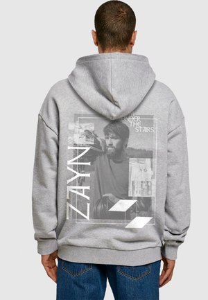 Grå hoodie med et stort trykt grafik på ryggen, der viser et sort-hvidt portræt og fed tekst. Blødt materiale, løstsiddende pasform.