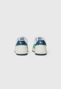 Een paar witte, groene en blauwe lage Puma sneakers gezien vanuit de achterkant, met een gouden Puma-logo op de blauwe hieltab.