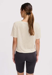 Lys beige kortærmet bluse med en blød tekstur, parret med mørkegrå tætsiddende shorts, der slutter over knæet. Enkel, afslappet design.
