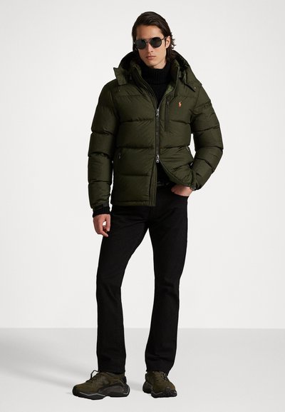 Opblaasparka in donkergroen met een ritssluiting, een afneembare capuchon en geribbelde manchetten. Gecombineerd met zwarte jeans en donkere sneakers.