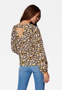 Schwarze Bluse mit floralem Muster in Gelb, Pink und Weiß, mit Puffärmeln und einem Schlüssel-Ausschnitt hinten. Legerer, leichter Stoff.