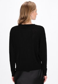 Maglione nero oversize con maniche lunghe e orlo a costine. Tessuto morbido e leggero con una sottile texture. Vista da dietro.