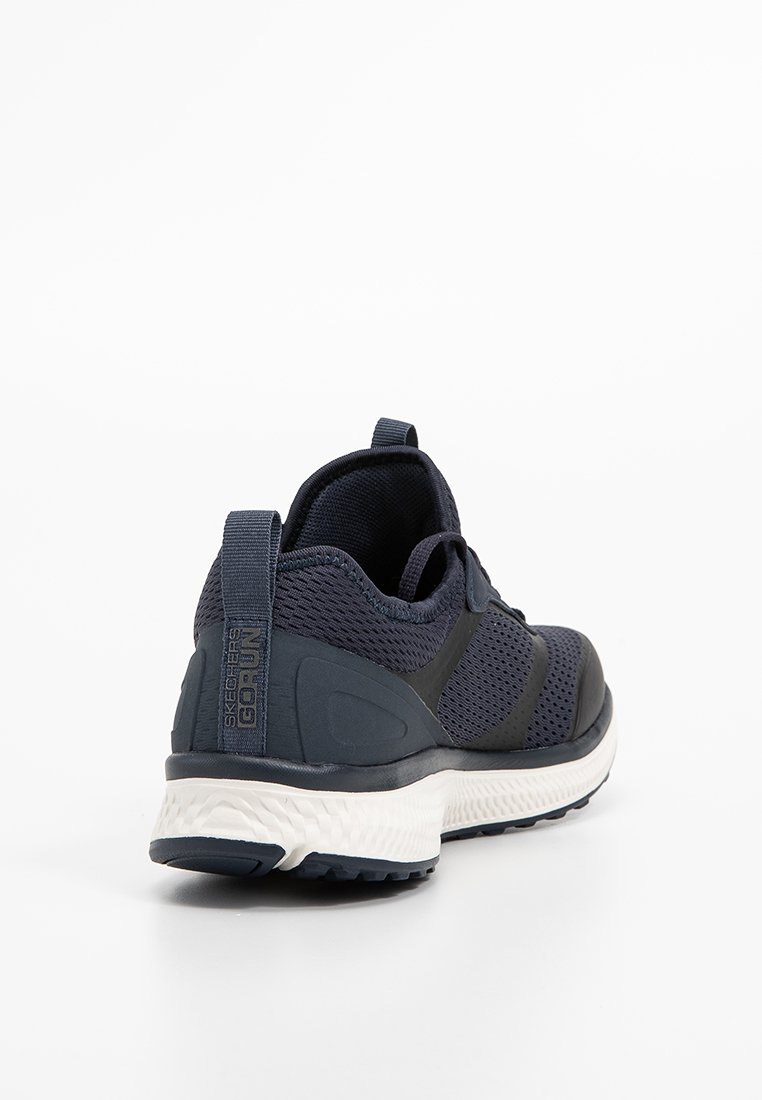 Chaussure de sport en marine foncé avec tige en mesh, col rembourré et semelle en caoutchouc. Dispose d'une languette de tirage et d'accents texturés sur les côtés.