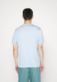 Svetle modré tričko s krátkým rukávem vyrobené z měkkého materiálu, s kulatým výstřihem a malým logem na zádech. Jednoduchý design, bez vzorů.