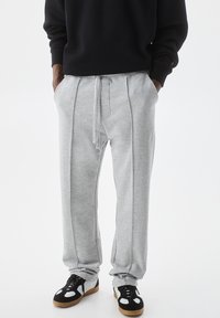 Gray sweatpants with a drawstring, featuring side seams, elastic cuffs, and pockets, paired with black and white sneakers.