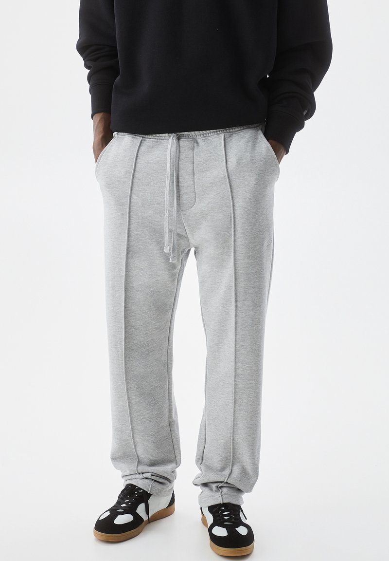 Gray sweatpants with a drawstring, featuring side seams, elastic cuffs, and pockets, paired with black and white sneakers.