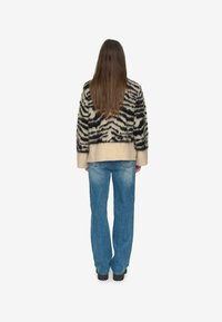 Wollen sweater met een zwart en crèmekleurig tijgerstreep patroon, gecombineerd met lichtblauwe wijde jeans en zwarte chunky-soled laarzen.