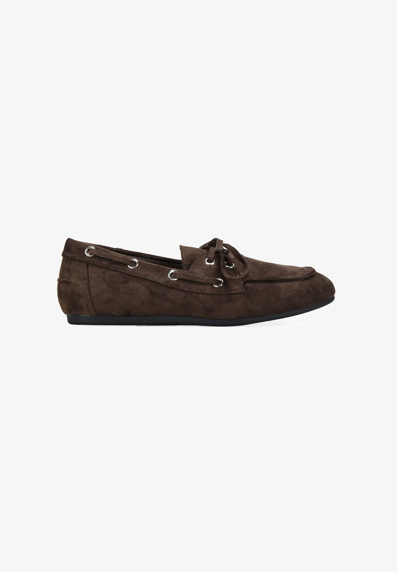 Zapato mocasín de ante marrón con punta redondeada, detalle de cordones y ojales de metal. Suela plana, textura suave y diseño sencillo.