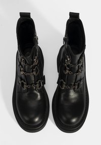 Bottines en cuir noir avec accents de chaînes et fermetures éclairs latérales. Caractérisées par une texture lisse et un bout arrondi, avec un intérieur rembourré.
