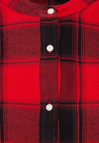 Chemise à carreaux rouge et noir à boutons, fabriquée en tissu tissé ; dotée de boutons blancs et d'un col rond avec une patte de boutonnage à l'avant.