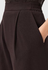 Pantaloni neri plissettati con tasche laterali, texture liscia e vita arricciata per comfort e design aderente.