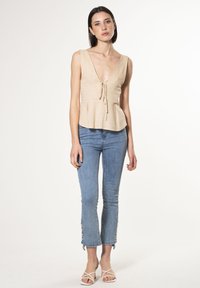 Top beige senza maniche con scollo a V, dettagli con cordoncino e orlo a peplo; abbinato a jeans cropped azzurri chiari con dettagli in bottoni.