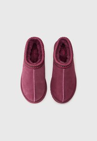 Chaussons en daim violet avec doublure en peluche, design à enfiler et surpiqûres décoratives contrastantes sur le col.  Bout arrondi et semelle plate.