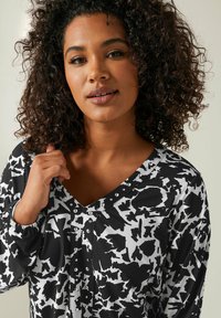 Blouse à motifs floraux en noir et blanc avec décolleté en V, accents de boutons et manches élastiquées. Tissu lisse avec un léger éclat.