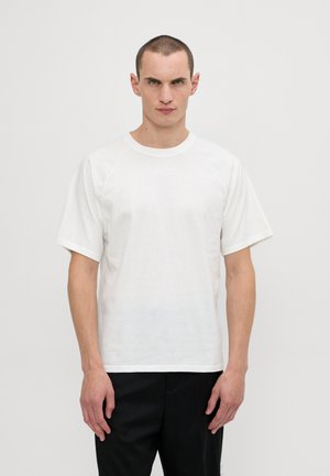 White, short-sleeve t-shirt made of cotton. Features a crew neckline and raglan sleeves, resting on a model against a plain background.