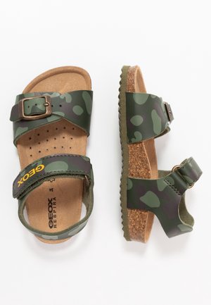 Zielone sandały w kamuflażowy wzór z dwiema regulowanymi tasiemkami, klamrą i korkową podeszwą. Miękka, teksturowana wkładka dla komfortu.