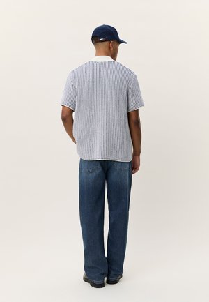 Γκρι ριγέ πουκάμισο με κοντά μανίκια και λευκό γιακά, συνδυασμένο με φαρδιά μπλε τζιν και σκούφο μπέιζμπολ σε ναυτικό μπλε. Απαλή υφή, άνετη εφαρμογή.