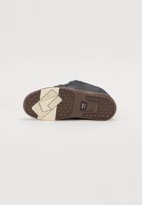 Fekete sneaker talp, textúrált barna gumimintával, fehér kiemeléssel és logóval. A talp kialakítása tapadást és támogatást nyújt.
