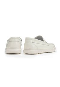 Zapatos blancos sin cordones fabricados en cuero texturizado con una suela de goma de perfil bajo. Punta redondeada con un detalle de costura mínima en la parte superior.