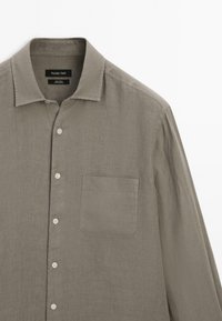 Light gray long-sleeve button-up shirt in linen fabric. Features a pointed collar, front pocket, and six buttons down the front.
