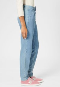 Hellblaue Jeans aus Denim mit geradem Bein, ausgestattet mit einem Bund mit Gürtelschlaufen und Seitentaschen, kombiniert mit pinkfarbenen Schnürschuhen.