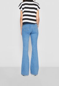 Černo-bílý pruhovaný crop top s krátkými rukávy, zkombinovaný se světle modrými zvonovými džínami a bílou obuví. Zobrazen pohled zezadu.