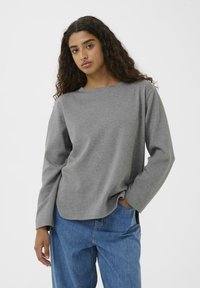 Maglia grigia a maniche lunghe con scollo rotondo e vestibilità rilassata. Realizzata in tessuto morbido, abbinata a jeans blu a vestibilità ampia.