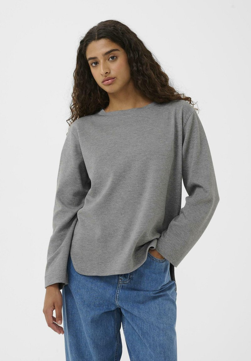 Maglia grigia a maniche lunghe con scollo rotondo e vestibilità rilassata. Realizzata in tessuto morbido, abbinata a jeans blu a vestibilità ampia.