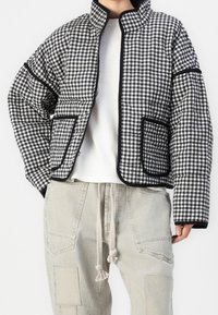 Prošívaná černobílá kostkovaná bunda s vysokým límcem, kontrastním černým lemem a dvěma předními kapsami. Nositá přes bílý top.