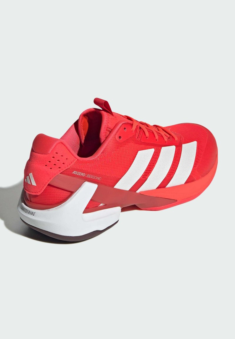 Baskets de sport rouges avec tige en maille, accents de rayures blanches, surface texturée et semelle contrastante blanche et marron. Dispose d'une languette.
