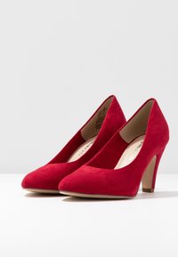 Scarpe con tacco alto in suede rosso, dalla punta affilata e tacco sottile e visibile. Parte superiore liscia con una texture morbida e dettagli minimi.