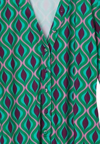 Camicia colorata con un motivo geometrico verde, teal e bordeaux caratterizzato da forme appuntite. Realizzata in tessuto morbido con bottoni davanti.